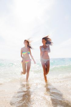 Two young and attractive women in bikini running by the beach