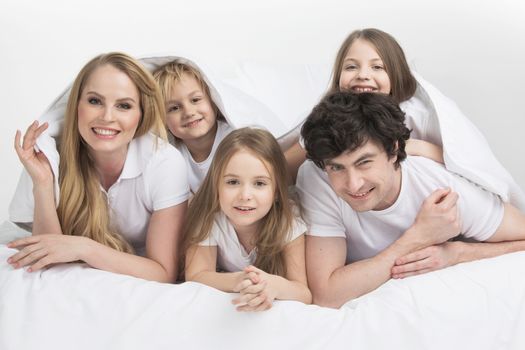 Smiling family with three children wake up in bed