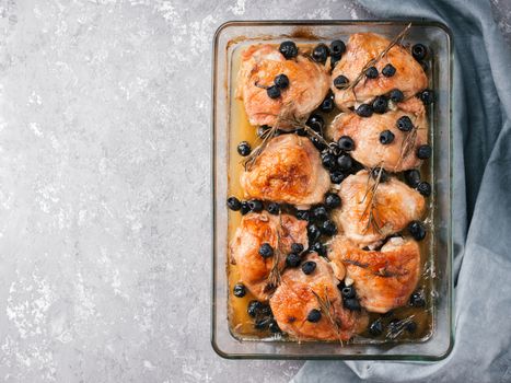 Corsican chicken thighs with rosemary, black olives, garlic in lemon juice and wine. Chicken legs cooked in oven on gray concrete background. Baked chicken leg in heat-proof glass. Top view.Copy space