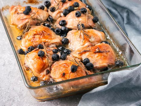 Corsican chicken thighs with rosemary, black olives, garlic in lemon juice and wine. Chicken legs cooked in oven on gray concrete background. Baked chicken leg in heat-proof glass. Copy space
