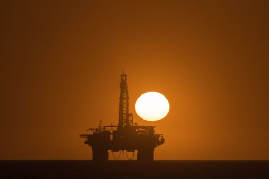 The sun is setting over an oil drilling platform anchored in the Atlantic Ocean at Longbeach in the Namib Desert of Namibia
