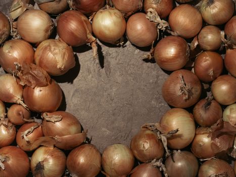 Fresh yellow onions on brown concrete background. Onions with copy space in circle form. Hard light. Low key. Top view.