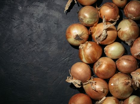 Fresh yellow onions on black concrete background. Onions with copy space. Fresh onions in low key. Hard light. Top view.