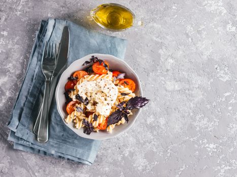 Tasty italian fusilli pasta with cherry, mozarella or buratta cheese and fresh basil. Dish with pasta on gray concrete background. Top view. Copy space. Healthy food concept and recipe idea.