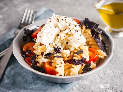 Tasty italian fusilli pasta with cherry, mozarella or buratta cheese and fresh basil. Dish with pasta on gray concrete background. Copy space. Healthy food concept and recipe idea.