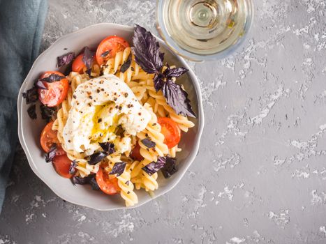 Tasty italian fusilli pasta with cherry, mozarella or buratta cheese and fresh basil. Dish with pasta on gray concrete background. Top view. Copy space. Healthy food concept and recipe idea.