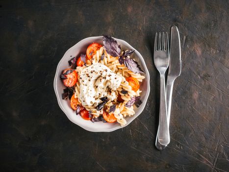 Tasty italian fusilli pasta with cherry, mozarella or buratta cheese and fresh basil. Dish with pasta on black concrete background. Top view. Copy space. Healthy food concept and recipe idea.