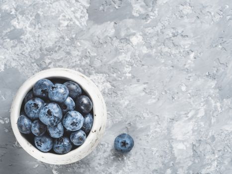 Blueberries on gray concrete background. Blueberry border design. Fresh picked bilberries in bowl close up. Copyspace. Top view or flat lay