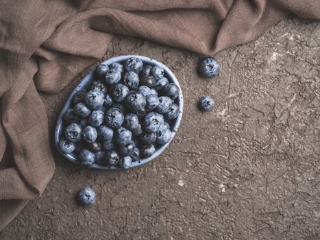 Blueberries in plate on brown concrete background. Fresh picked bilberries close up. Copyspace. Top view or flat lay