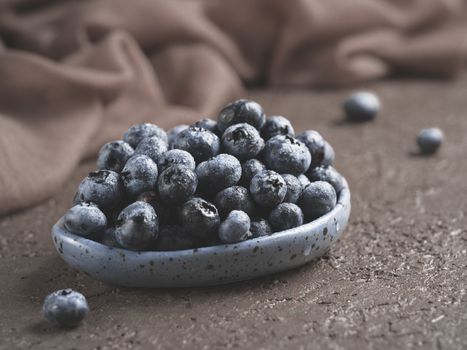 Blueberries in plate on brown concrete background. Fresh picked bilberries close up. Copyspace. Close up