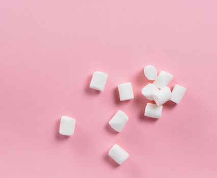 Marshmallows on pink background with copyspace. Flat lay or top view. Background or texture of colorful mini marshmallows. Winter food background concept.