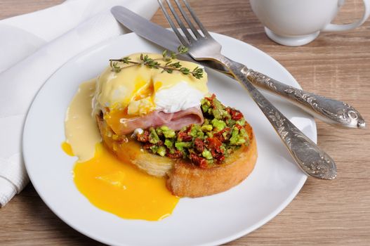Toasted baguette slice with guacamole, ham and eggs Benedict under Dutch sauce