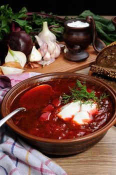 Borscht-vegetable beetroot soup, on the table with slices of rye cereal bread and gluten of sour cream, garlic and herbs. Rustic style.