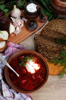Borscht-vegetable beetroot soup, on the table with slices of rye cereal bread and gluten of sour cream, garlic and herbs. Rustic style.