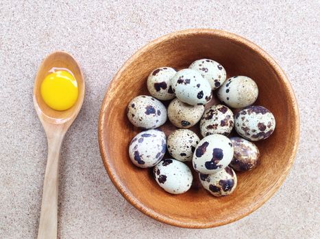Quail eggs in wooden bowl and egg yolk in wooden spoon