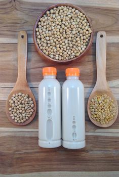 Soy milk in bottle and soy beans with wooden ladle on wooden background