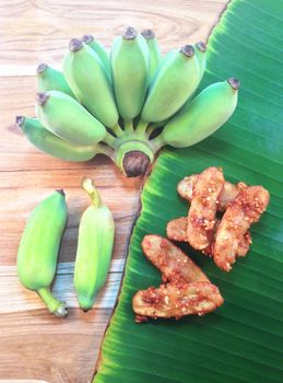 Green cultivated banana and fried banana on wooden and banana leaf background