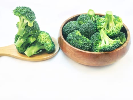 Broccoli in wooden bowl and wooden spoon on white background