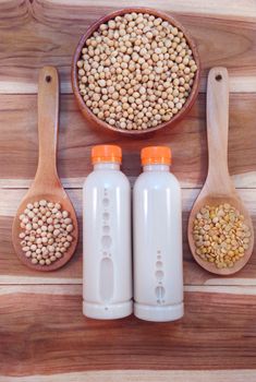 Soy milk in bottle and soy beans with wooden ladle on wooden background