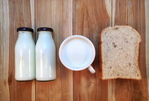 Slice of bread with bottle and cup of milk on wooden background