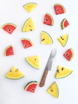 slices of red and yellow watermelon and knife on white background