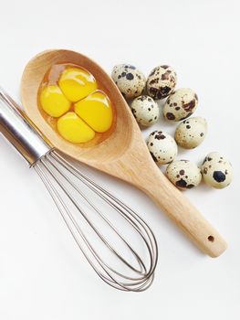 Quail eggs in wooden spoon and egg whisk on white background