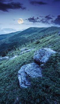 landscape with white sharp boulders on the hillside near mountain peak at night in full moon light
