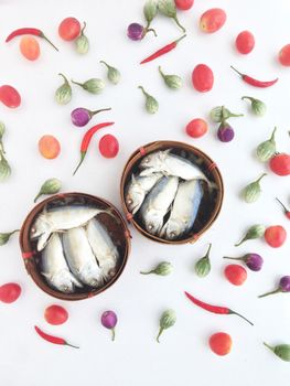 short mackerel on a round crate made of bamboo, used to transport fruits or fish, among vegetables