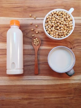 Soy milk in bottle and soy beans with wooden ladle on wooden background