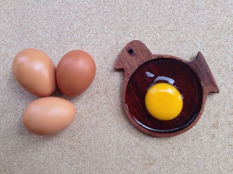 Egg yolk on wooden chicken shaped saucer and eggs on plywood