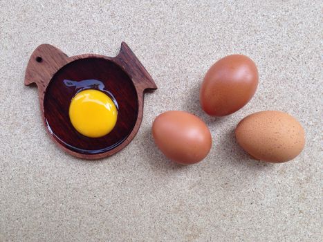 Egg yolk on wooden chicken shaped saucer and eggs on plywood