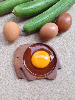 Yolk egg on wooden elephant shaped saucer with eggs and angle gourd on plywood background