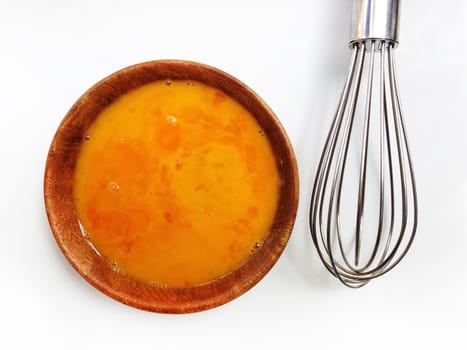 Fresh eggs in wooden bowl with egg whisk on white background