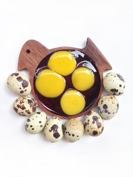 Quail eggs with yolk in wooden bird shaped saucer on white background