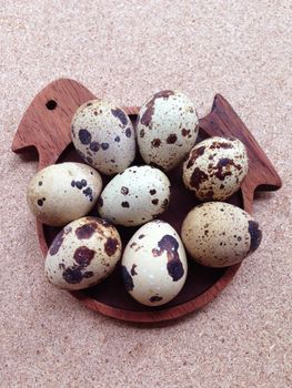 Quail eggs on wooden bird shaped saucer on plywood background