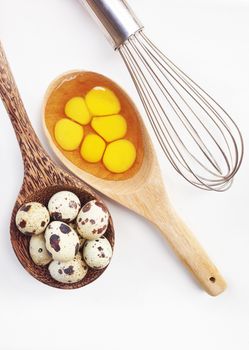 Quail eggs in wooden spoon and egg whisk on white background