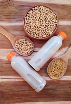 Soy milk in bottle and soy beans with wooden ladle on wooden background