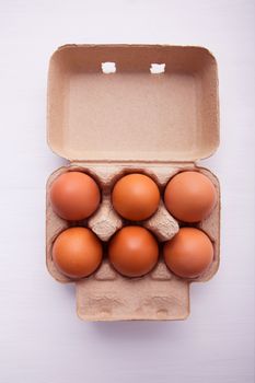 Chicken eggs in egg box on white wooden background.