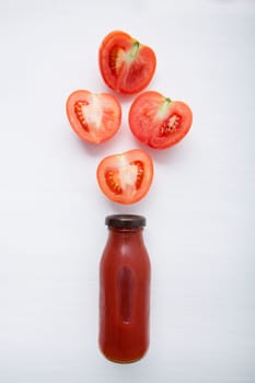 Tomatoes juice in bottle and fresh tomatoes slices on white wooden background.