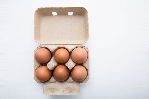 Chicken eggs in egg box on white wooden background.