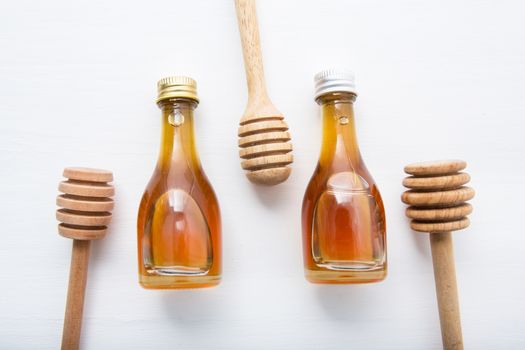 wooden dipper and little honey bottle on white wooden background.