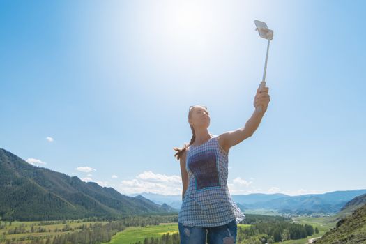 Woman taking selfie on mobile phone with stick. Vacation in the mountain