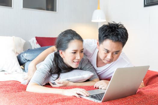 Young Asian Couples using laptop together in bedroom of contemporary house for modern lifestyle concept