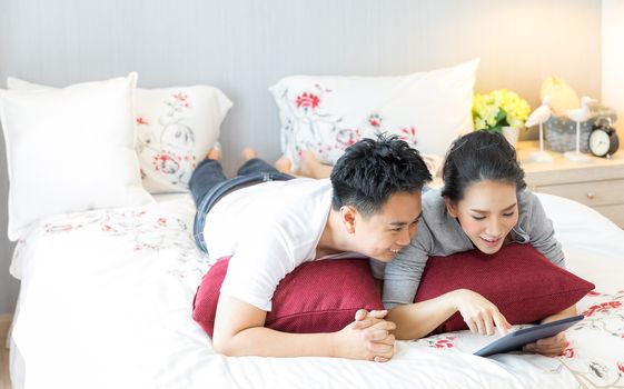 Young Asian Couples lying down and using tablet together in living room of contemporary house for modern lifestyle concept