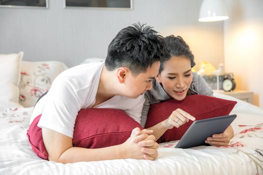 Young Asian Couples lying down and using tablet together in living room of contemporary house for modern lifestyle concept