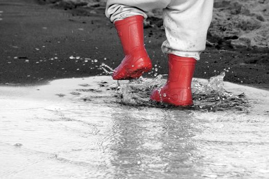 wellingtons in puddle.kid rubber boots in the sea background