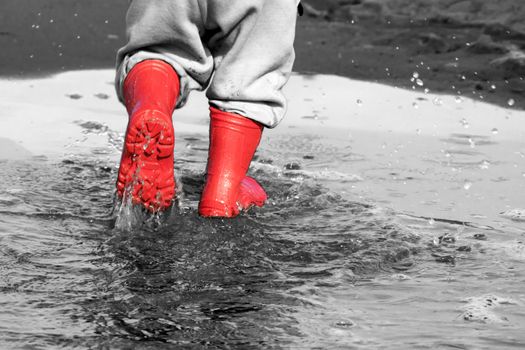 wellingtons in puddle.kid rubber boots in the sea background