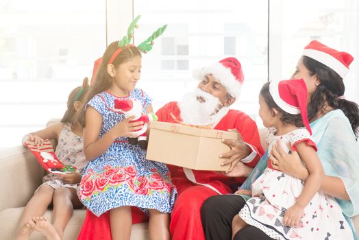 Happy Indian family celebrating Christmas holidays, with gift box and santa sitting on sofa or couch at home, Asian people festival mood indoors. 