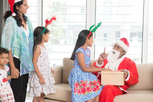 Happy Indian family celebrating Christmas holidays, with gift box and santa sitting on sofa at home, Asian people festival mood indoors. 