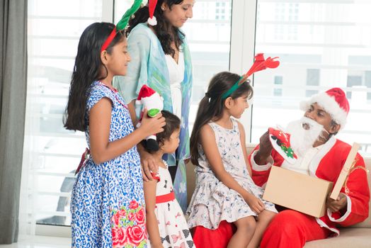 Happy Indian family celebrating Christmas holidays, with gift box and santa sitting on sofa or couch at home, Asian parents and children festival mood indoors. 